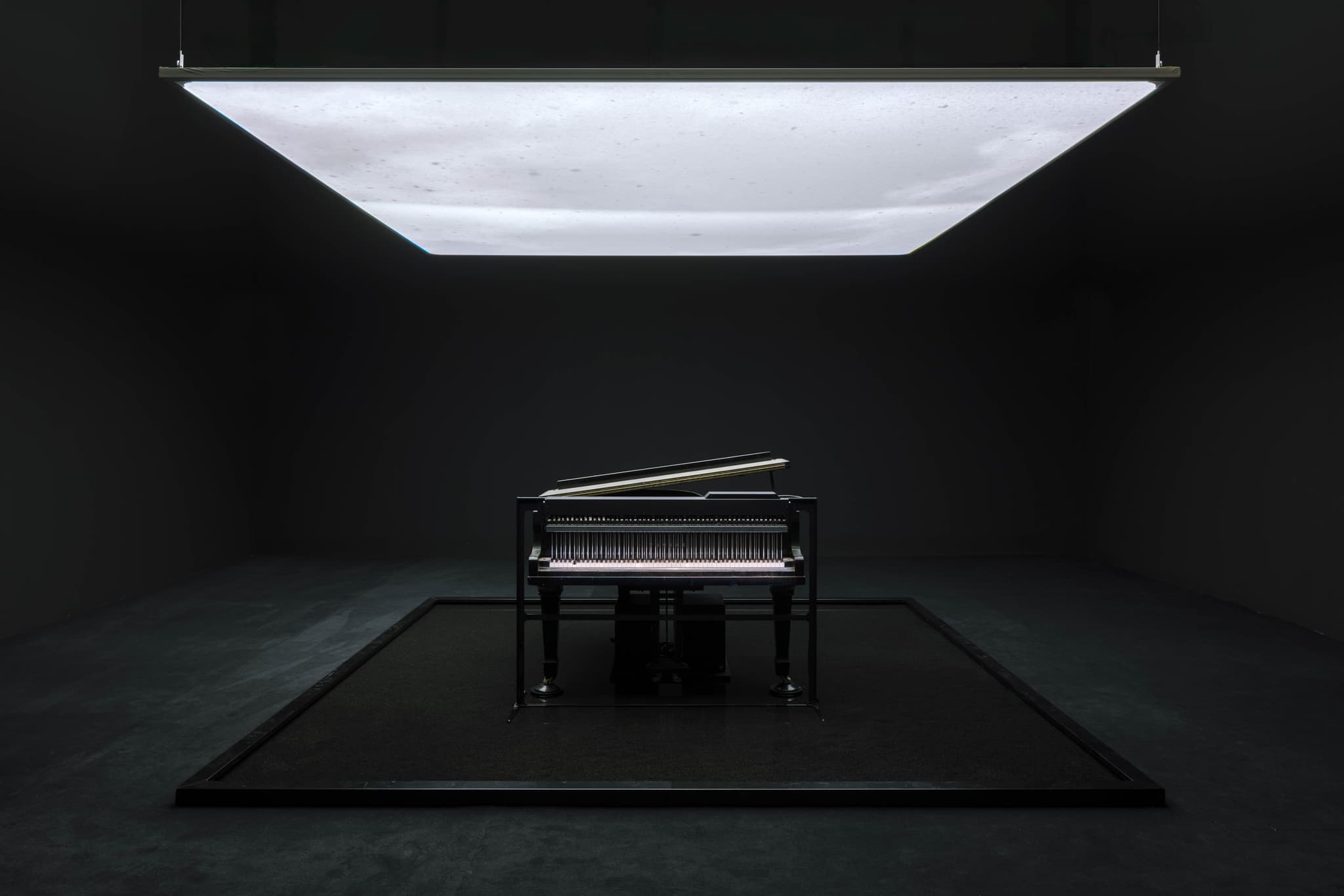 A tsunami-damaged piano stands beneath a glowing suspended water screen in Ryuichi Sakamoto and Shiro Takatani's IS YOUR TIME installation
